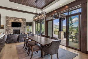 Dining space with a stone fireplace, light hardwood / wood-style flooring, a raised ceiling, and a healthy amount of sunlight