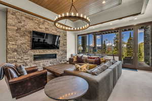 Carpeted living room with a fireplace, a tray ceiling, a notable chandelier, and wooden ceiling