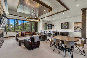 Carpeted living room featuring a raised ceiling, bar, a notable chandelier, and a fireplace