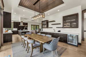 Dining space featuring wood ceiling, wine cooler, wet bar, a raised ceiling, and light wood-type flooring