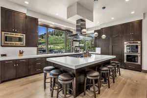 Kitchen featuring appliances with stainless steel finishes, island range hood, hanging light fixtures, a center island, and dark brown cabinetry