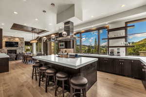 Kitchen featuring island range hood, dark brown cabinets, hanging light fixtures, light wood-type flooring, and a tray ceiling