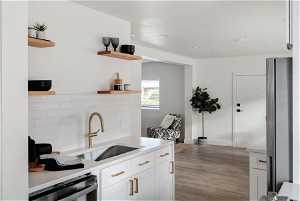 Kitchen featuring stainless steel appliances, tasteful backsplash, floating wood shelving, white cabinets, and sink