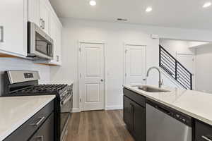 Kitchen featuring decorative backsplash, dark hardwood / wood-style flooring, white cabinetry, sink, and stainless steel appliances