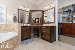 Primary bathroom with tiled bath, vanity, tile floors, and crown molding