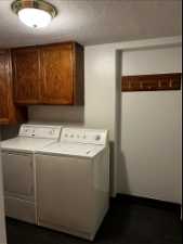 Laundry room with a textured ceiling, washer and clothes dryer, and cabinets