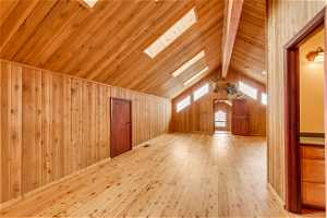 Bonus room with high vaulted ceiling, wooden walls, light hardwood / wood-style floors, a skylight, and beamed ceiling