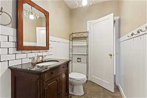 Bathroom featuring toilet, oversized vanity, a notable chandelier, tile floors, and backsplash