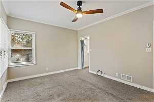 Carpeted empty room featuring ceiling fan and ornamental molding