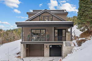 Modern home featuring stone siding, a garage, concrete driveway, and a balcony