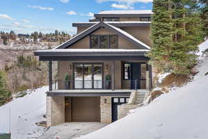 View of front of property with covered porch, a garage, stairway, and stone siding