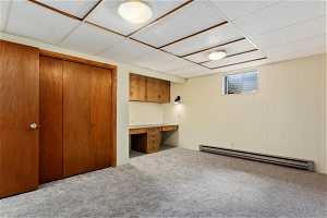 Basement featuring built in desk, baseboard heating, carpet floors, and a drop ceiling