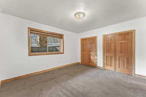 Unfurnished bedroom with two closets, a textured ceiling, and carpet flooring