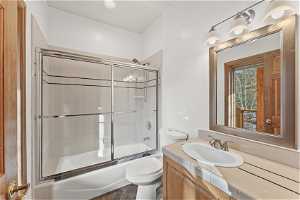 Full bathroom with toilet, tile floors, shower / bath combination with glass door, and vanity