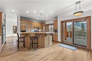 Kitchen with wood counters, light hardwood / wood-style floors, a kitchen bar, double oven, and decorative light fixtures