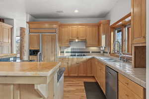 Kitchen featuring tile counters, sink, appliances with stainless steel finishes, tasteful backsplash, and light wood-type flooring