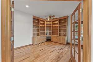Unfurnished office with light wood-type flooring, ceiling fan, and built in desk