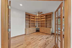 Unfurnished office with light wood-type flooring, ceiling fan, and built in desk