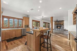 Kitchen with sink, light hardwood / wood-style flooring, stainless steel dishwasher, hanging light fixtures, and a stone fireplace