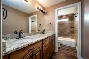 Full bathroom with tiled shower / bath, toilet, wood-type flooring, and dual vanity