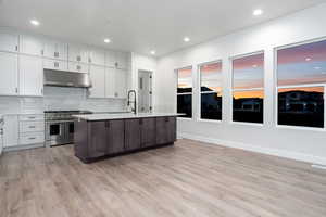 Kitchen with double oven range, white cabinetry, an island with sink, and light hardwood / wood-style flooring