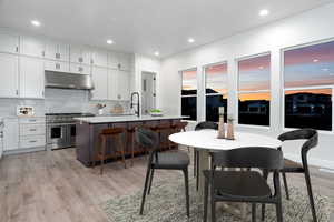 Kitchen with backsplash, a kitchen island with sink, white cabinets, and double oven range