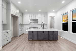 Kitchen featuring sink, stainless steel range oven, an island with sink, white cabinets, and light wood-type flooring