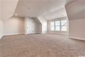 Additional living space with light colored carpet and vaulted ceiling