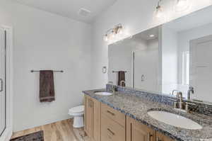 Bathroom with toilet, vanity with extensive cabinet space, double sink, a shower with door, and hardwood / wood-style floors