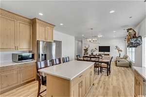 Kitchen featuring a breakfast bar area, a chandelier, appliances with stainless steel finishes, light hardwood / wood-style floors, and a kitchen island