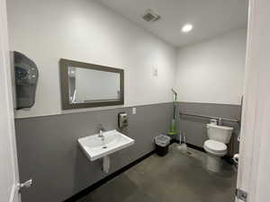 Bathroom featuring toilet, sink, and concrete flooring