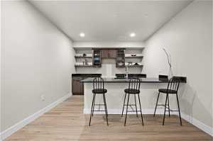 Kitchen with sink, light hardwood / wood-style floors, a breakfast bar area, dark brown cabinets, and kitchen peninsula