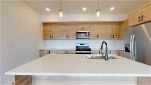 Kitchen with a center island with sink, appliances with stainless steel finishes, and decorative light fixtures