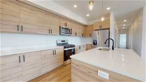 Kitchen with pendant lighting, light wood-type flooring, a kitchen island with sink, and stainless steel appliances