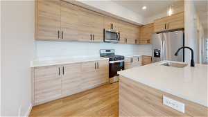 Kitchen with sink, pendant lighting, stainless steel appliances, light wood-type flooring, and light brown cabinetry