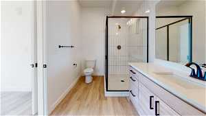 Bathroom featuring toilet, wood-type flooring, vanity with extensive cabinet space, and an enclosed shower
