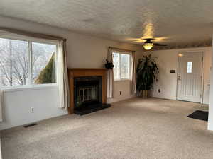 Unfurnished living room with a textured ceiling, ceiling fan, a premium fireplace, and light carpet