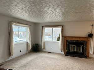 Unfurnished living room featuring a premium fireplace, a textured ceiling, and light colored carpet