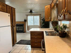 Kitchen featuring a fireplace, white fridge, ceiling fan, a textured ceiling, and light tile floors