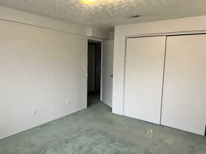 Unfurnished bedroom with dark carpet, a closet, and a textured ceiling