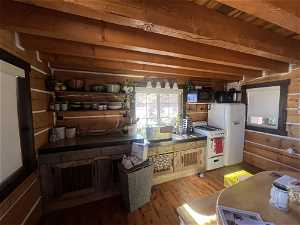 Bunk House. Kitchen with white appliances, wooden walls, light hardwood / wood-style flooring, and beam ceiling
