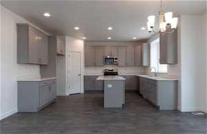 Kitchen featuring an inviting chandelier, appliances with stainless steel finishes, sink, a kitchen island, and dark wood-type flooring