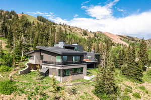 Back of house featuring a chimney, a view of trees, a mountain view, and a balcony