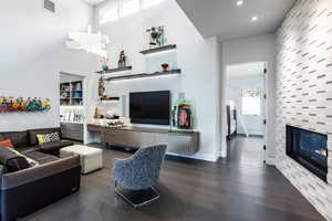 Living area with dark wood-style flooring, a tile fireplace, recessed lighting, and a towering ceiling