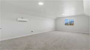 Additional living space featuring vaulted ceiling, light colored carpet, and a wall unit AC