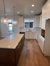 Kitchen with light wood-type flooring, white cabinetry, hanging light fixtures, a kitchen island, and backsplash