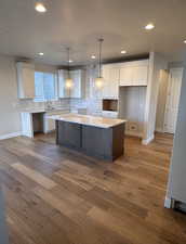 Kitchen with wood-type flooring, hanging light fixtures, a center island, and white cabinetry