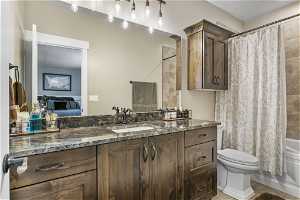 En-suite full bathroom with vanity, granite countertops, shower / bath combination with curtain, toilet, and tile flooring