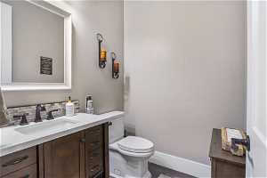 Powder room featuring hardwood / wood-style flooring, toilet, vanity with extensive cabinet space, and backsplash