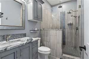 En-suite bathroom featuring vanity, granite countertops, toilet, and a tile shower